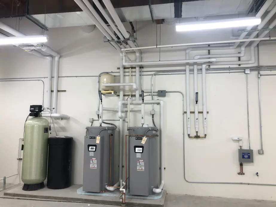 Two commercial water heaters and a water softener with insulated piping in a mechanical room