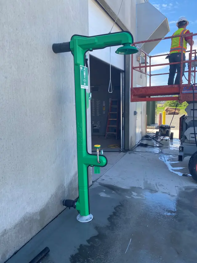 Green emergency shower and eye wash station installed on an exterior wall of a commercial building