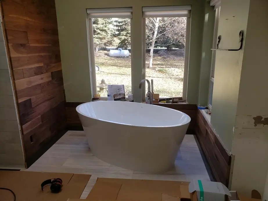 Freestanding tub with a floor-mount filler beside a reclaimed-wood wall, job in progress
