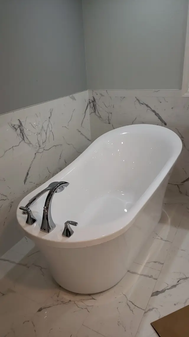 Freestanding soaker tub with a deck-mounted filler in marble-look tile