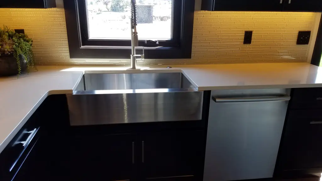 Farmhouse sink between dark cabinets with a dishwasher beside it