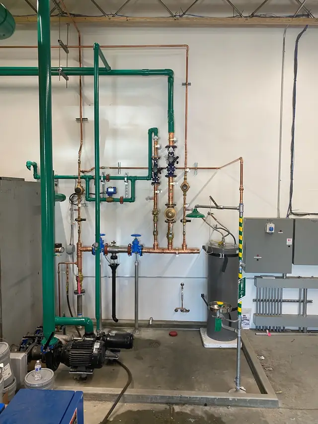 Green painted piping risers with copper branches, valves and a pump in a commercial mechanical room
