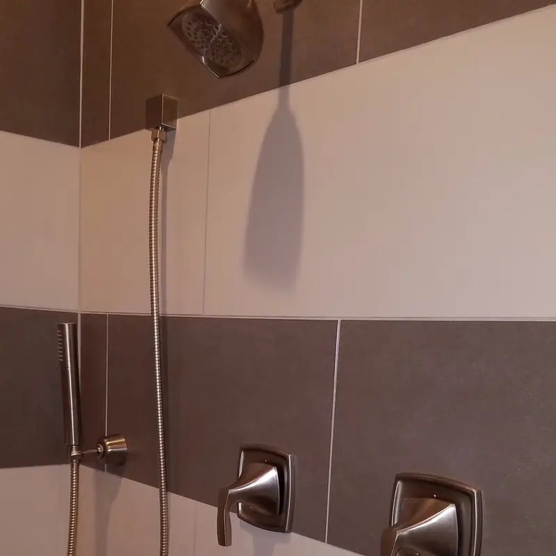 Custom shower with a hand shower on a slide bar and two valve trims in banded grey and white tile